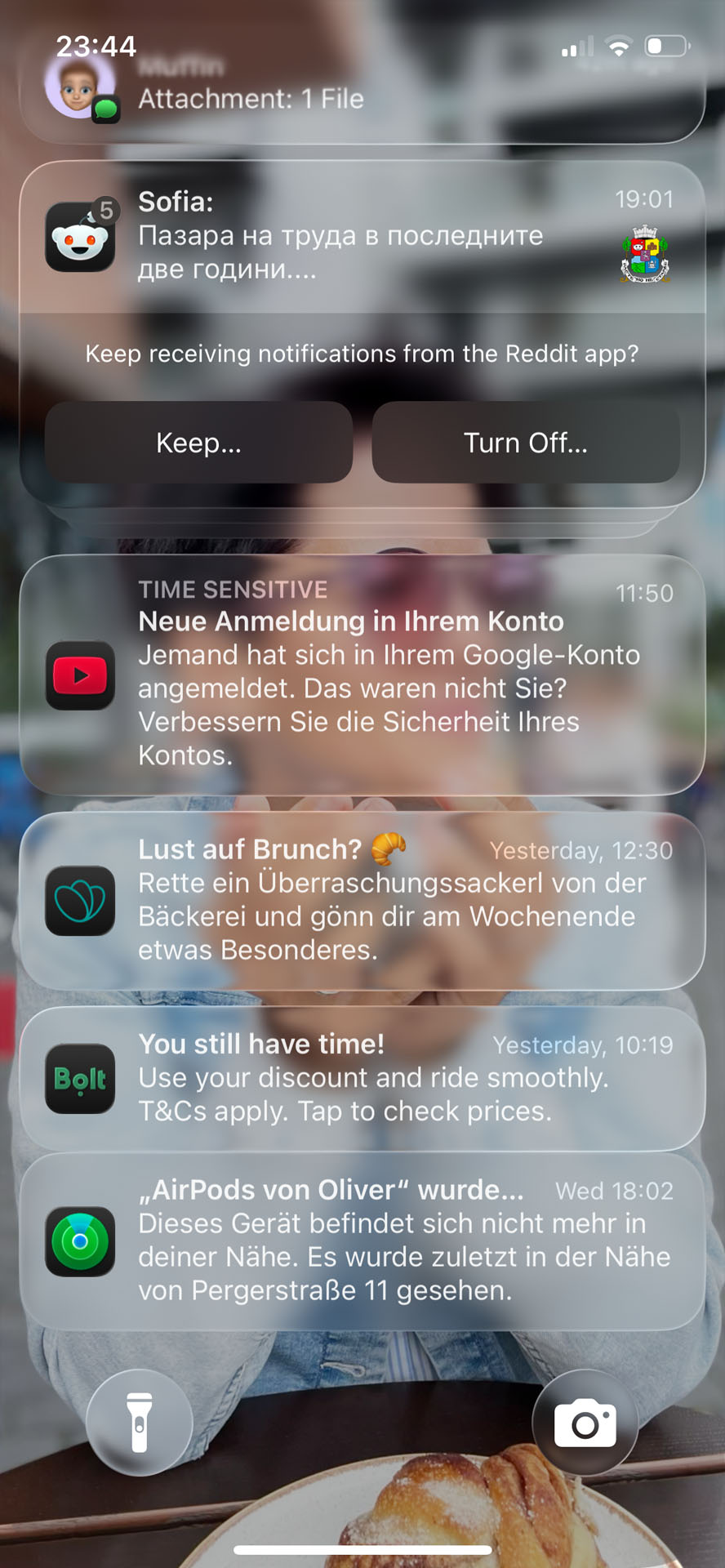 A screenshot of an iPhone lock screen running iOS 26, with a custom photo as a background. It is displaying multiple stacked notifications. The white text on the notifications on a partially blurred background is difficult to read due to low contrast and overlapping transparency effects.