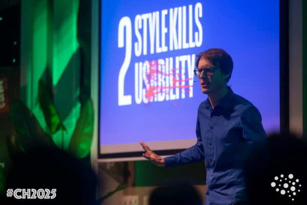 A speaker in a blue shirt addresses an audience in front of a blue slide that reads: "2 Style Kills Usability"