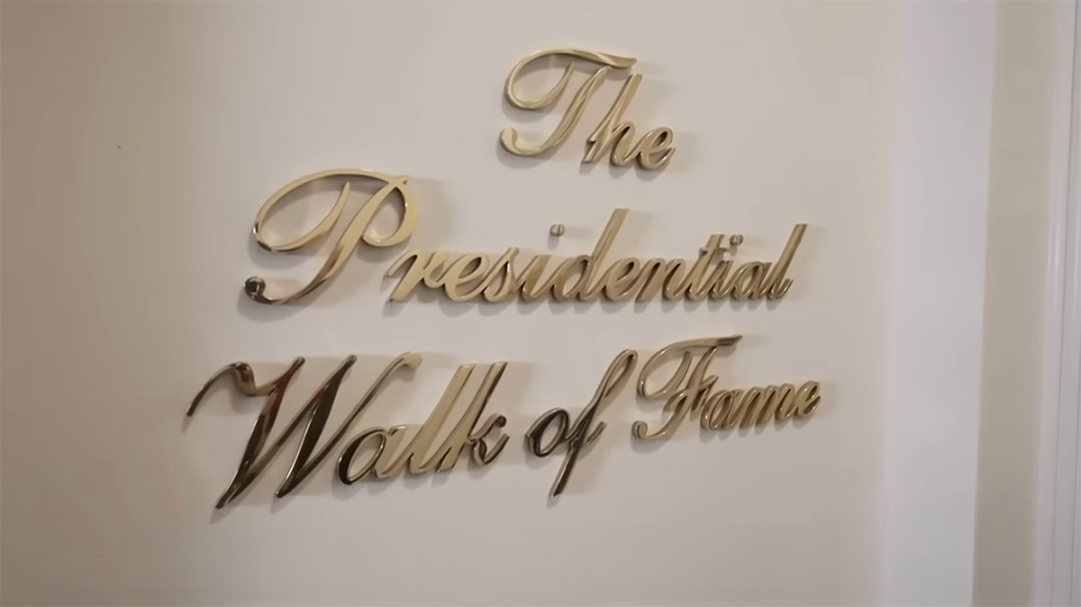 Gilded script letters mounted on a white wall reading “The Presidential Walk of Fame.”
