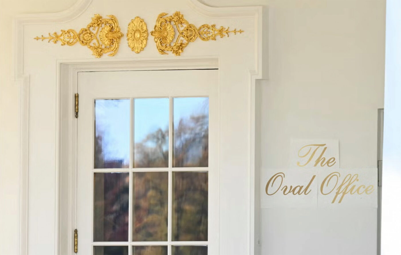 A paper signs mounted on a wall next to the entrance to the Oval Office from the rose garden. It is showing “The Oval Office“ in a gilded script font.